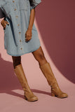 Woman wearing a light blue denim dress and brown knee-high boots against a pink background