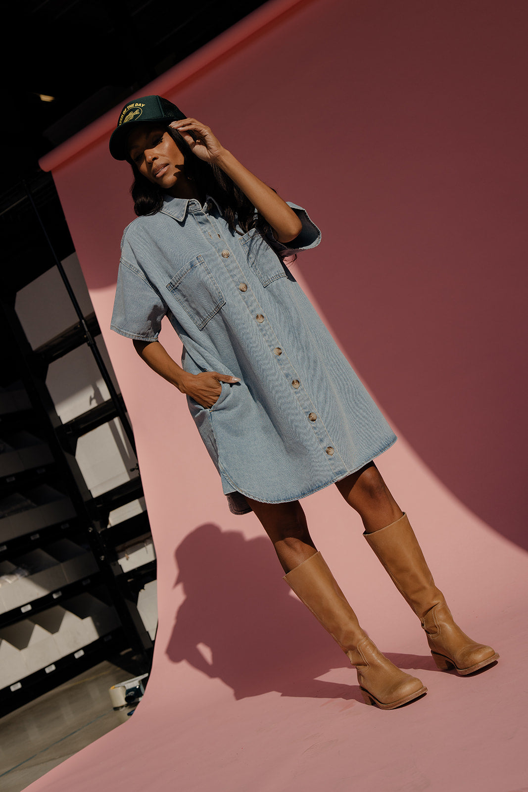 Woman wearing a light blue denim dress and brown boots on a pink background