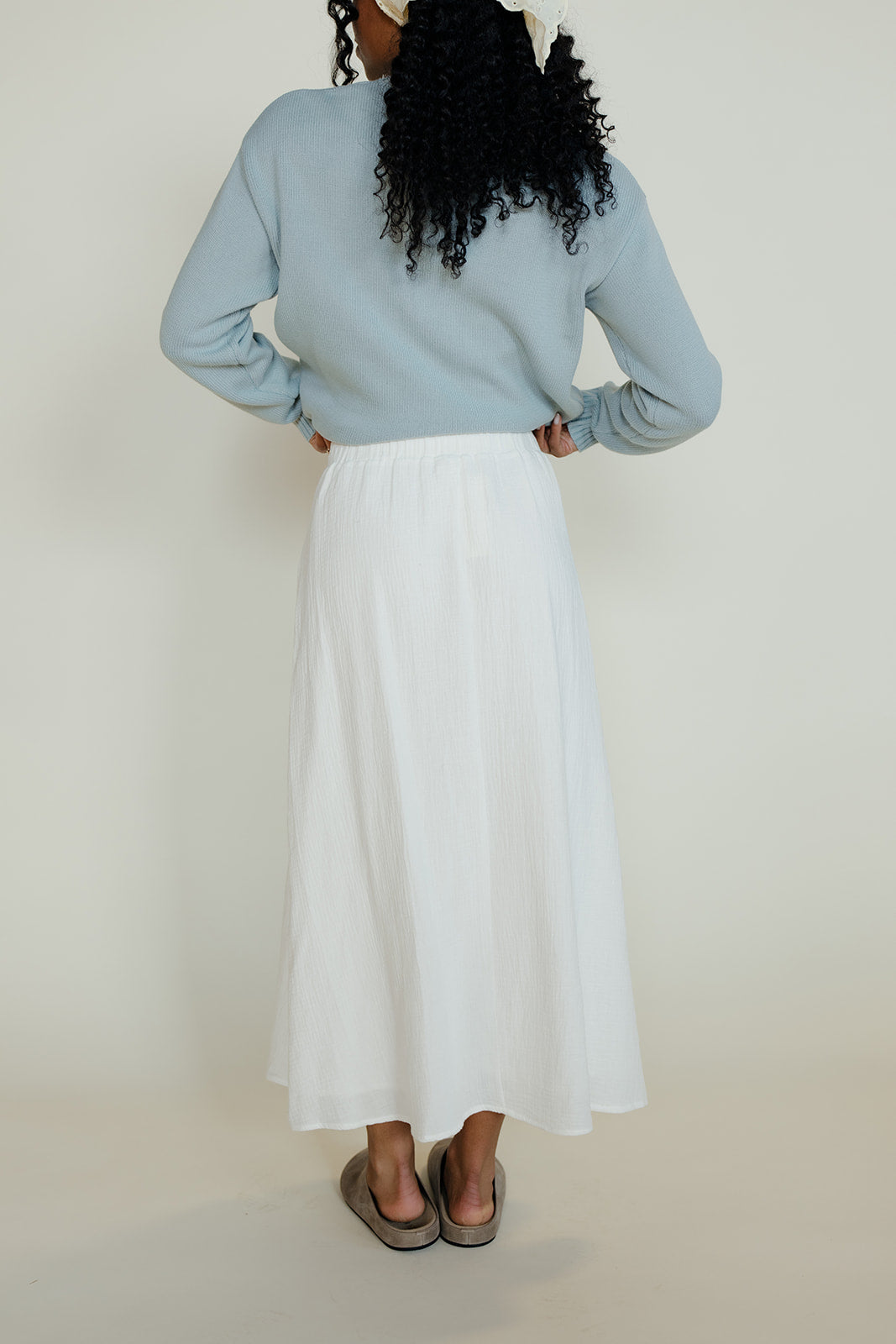 Person wearing a light blue sweater and white skirt against a plain background
