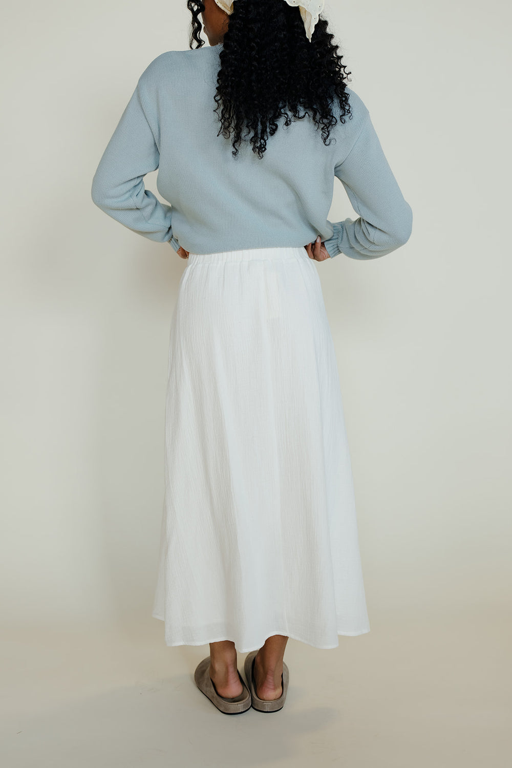 Person wearing a light blue sweater and white skirt against a plain background