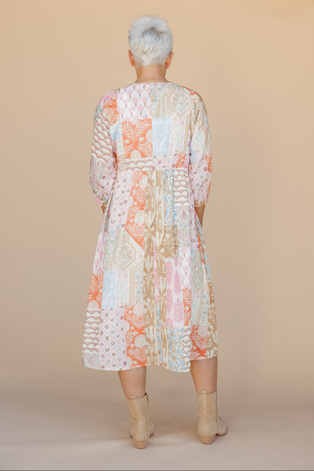 Person wearing a floral dress with long sleeves against a beige background