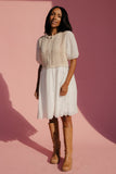 Woman wearing a white dress and brown boots against a pink background