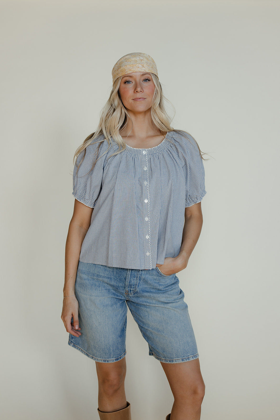 Woman wearing a light blue blouse and denim shorts against a plain background