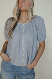 Woman wearing a blue checkered blouse with short sleeves against a plain background