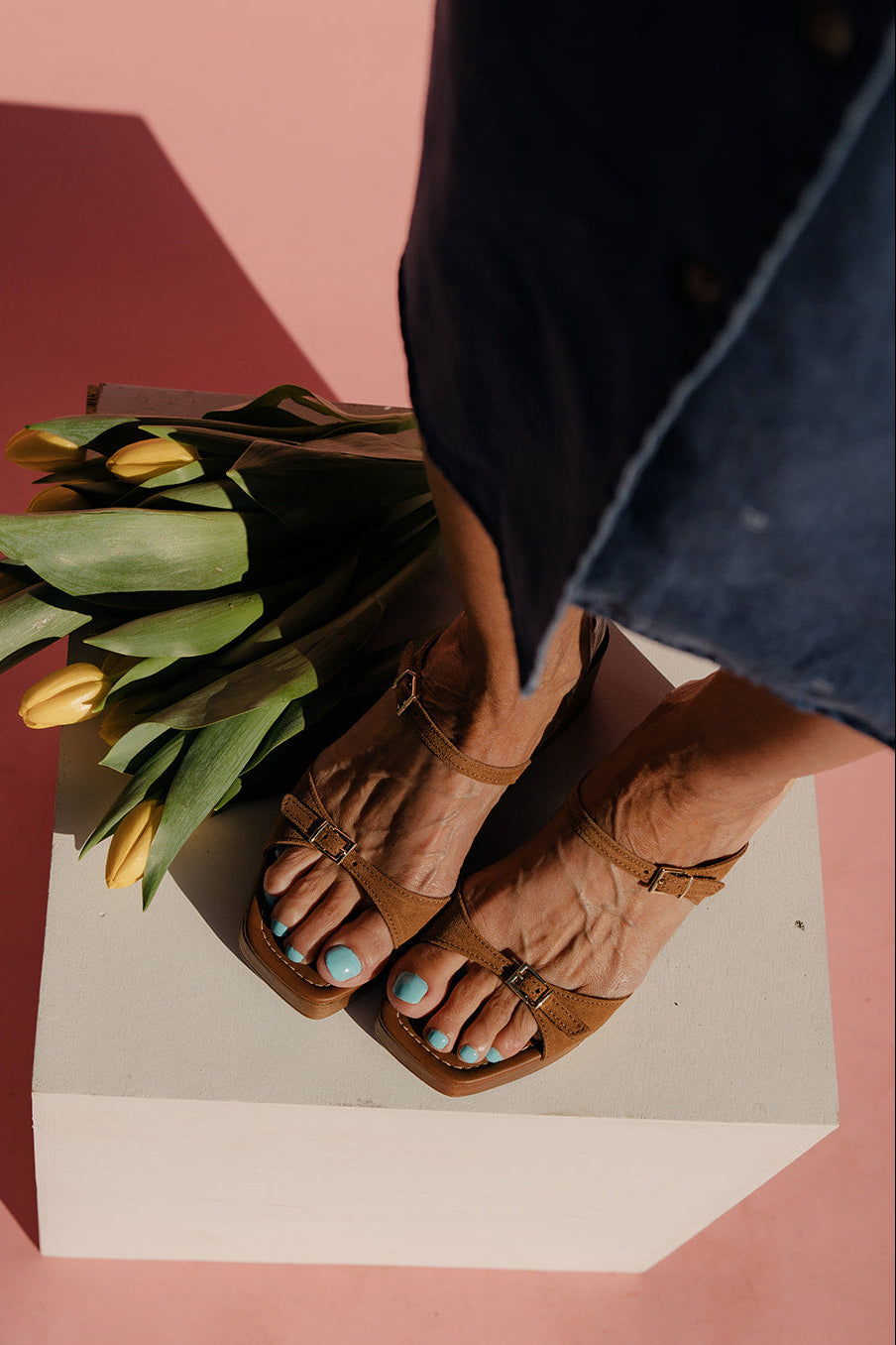 Person holding a bouquet of tulips with feet wearing brown sandals on a pink and white background
