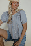Woman wearing a blue checkered blouse and denim shorts against a plain background