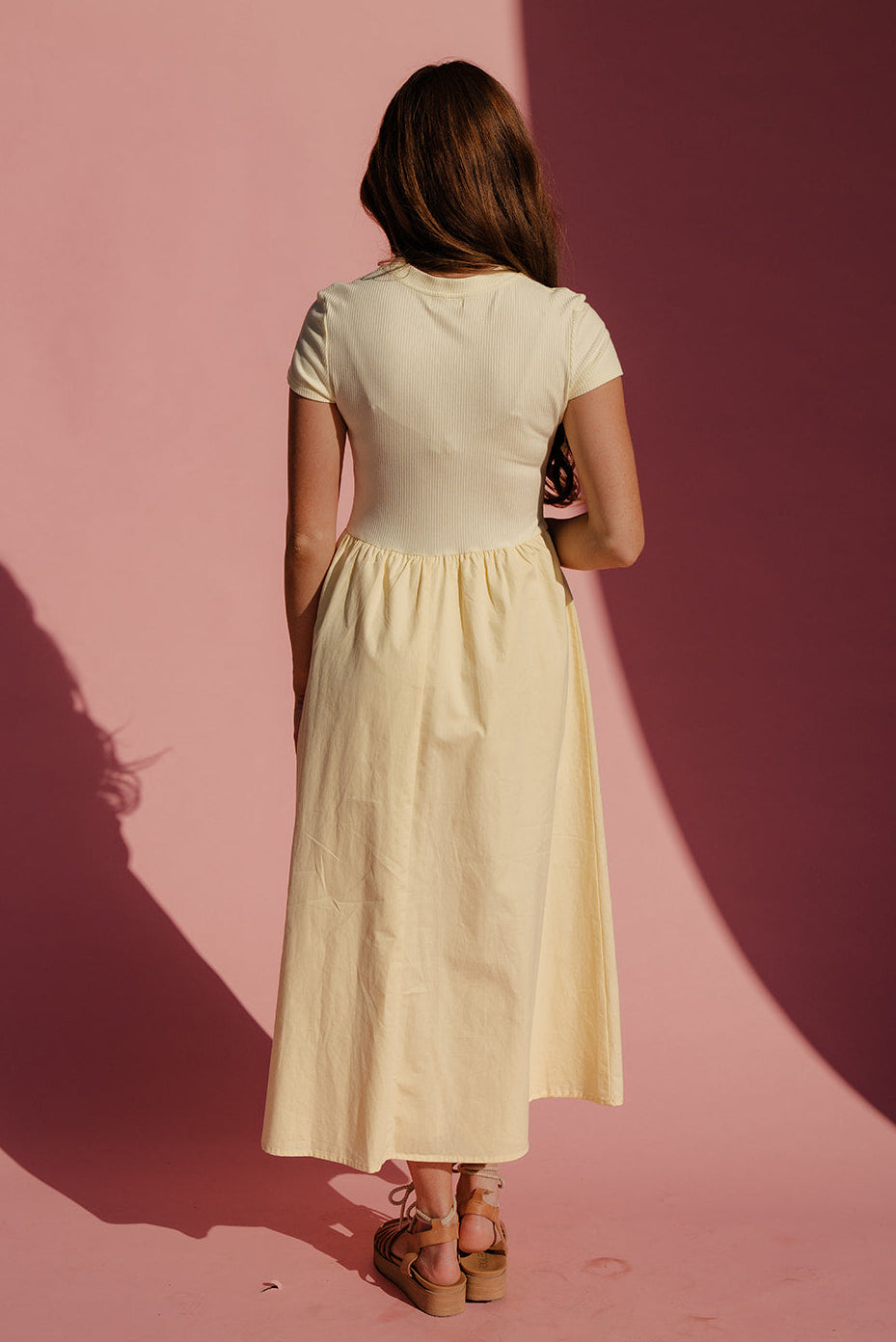 Woman in a white dress standing against a pink background