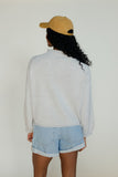 Person wearing a yellow cap, light gray sweater, and light blue shorts against a white background