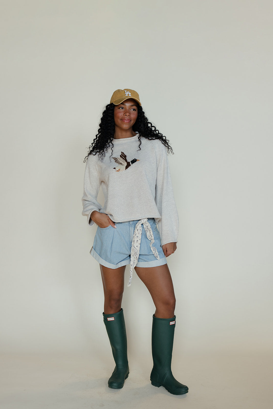 Person wearing a light gray sweatshirt, denim shorts, and green rain boots against a white background