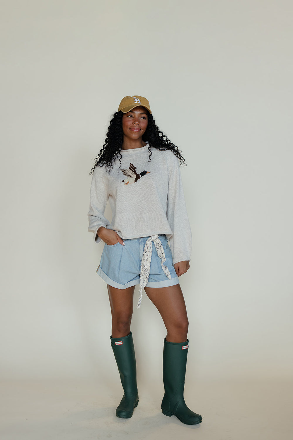Person wearing a light gray sweatshirt, denim shorts, and green rain boots against a white background