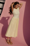 Woman in a white sleeveless top and beige skirt standing against a pink background