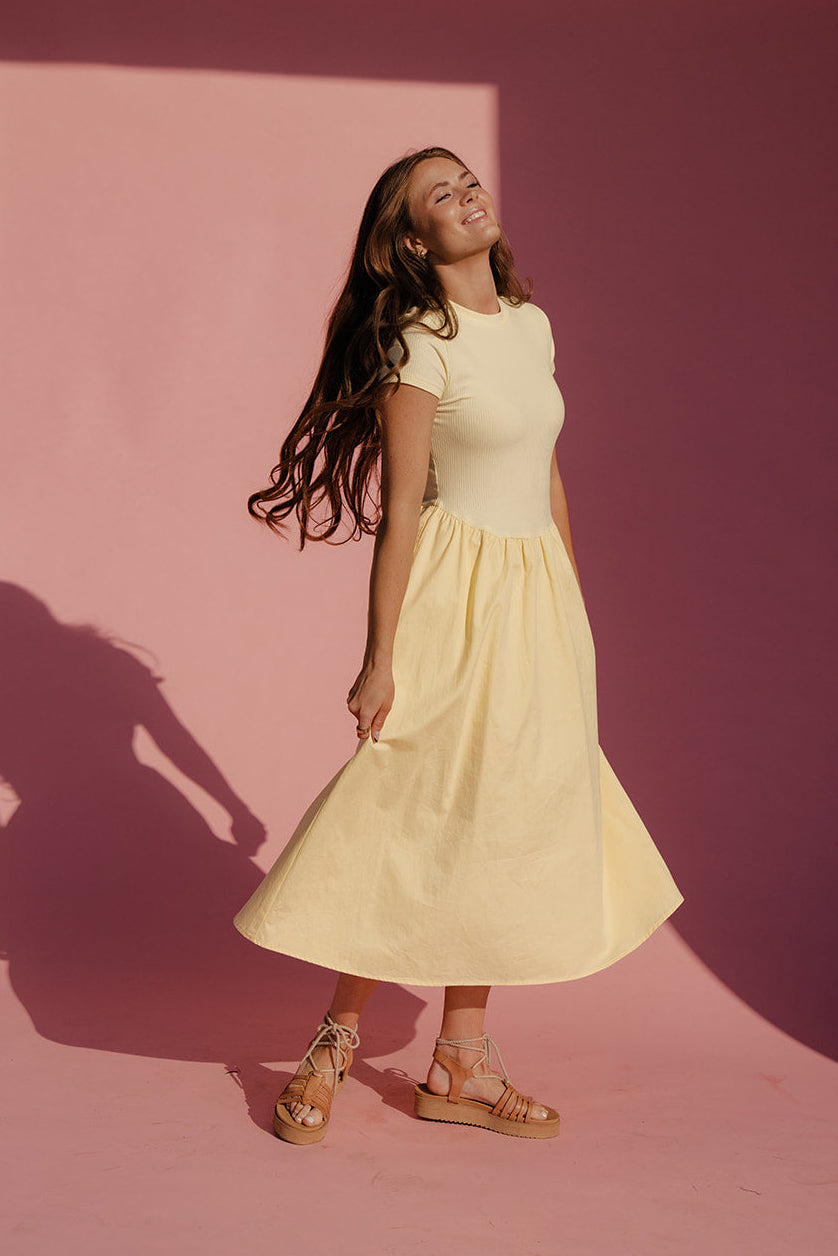 Woman in a yellow dress standing against a pink wall with a soft focus background