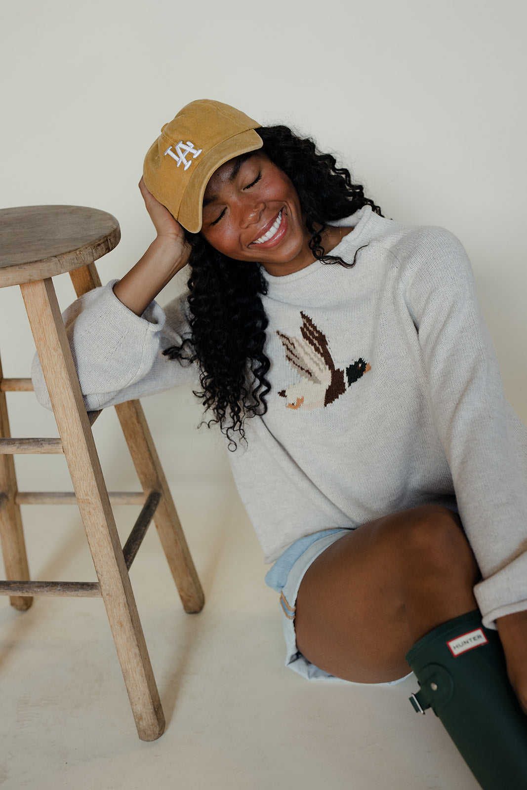 Woman wearing a gray sweatshirt with a graphic design, sitting on the floor next to a wooden stool.