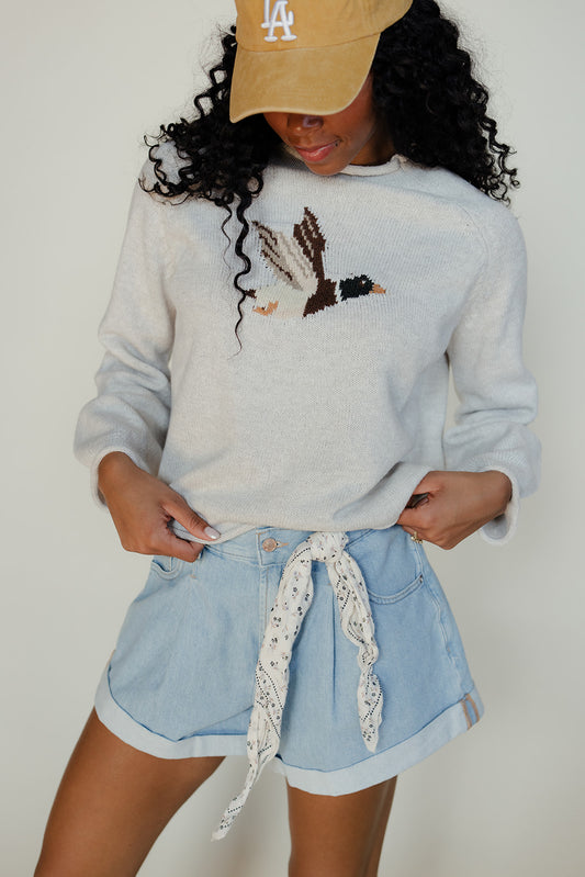 Person wearing a light blue sweater with a design, denim shorts, and a beige cap with 'LA' logo.