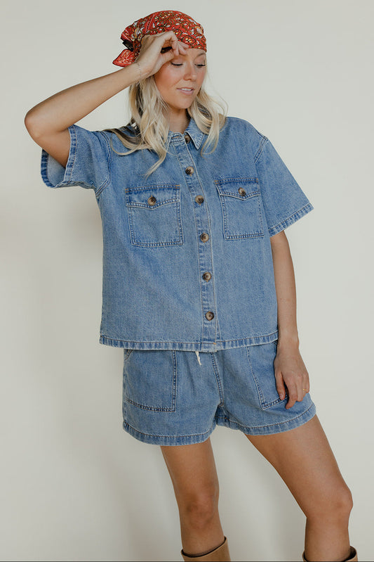 Person wearing a denim outfit with a headscarf against a plain background