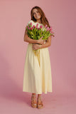 Woman in a yellow dress holding tulips against a pink background