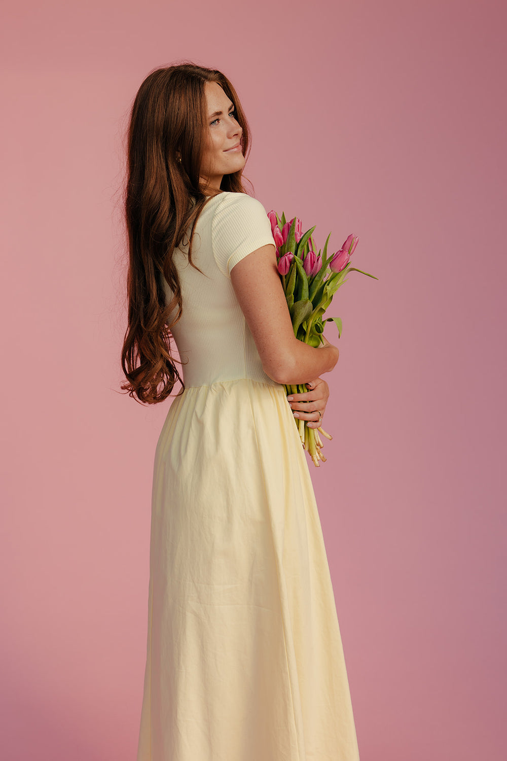 Woman in a white dress holding pink tulips against a pink background