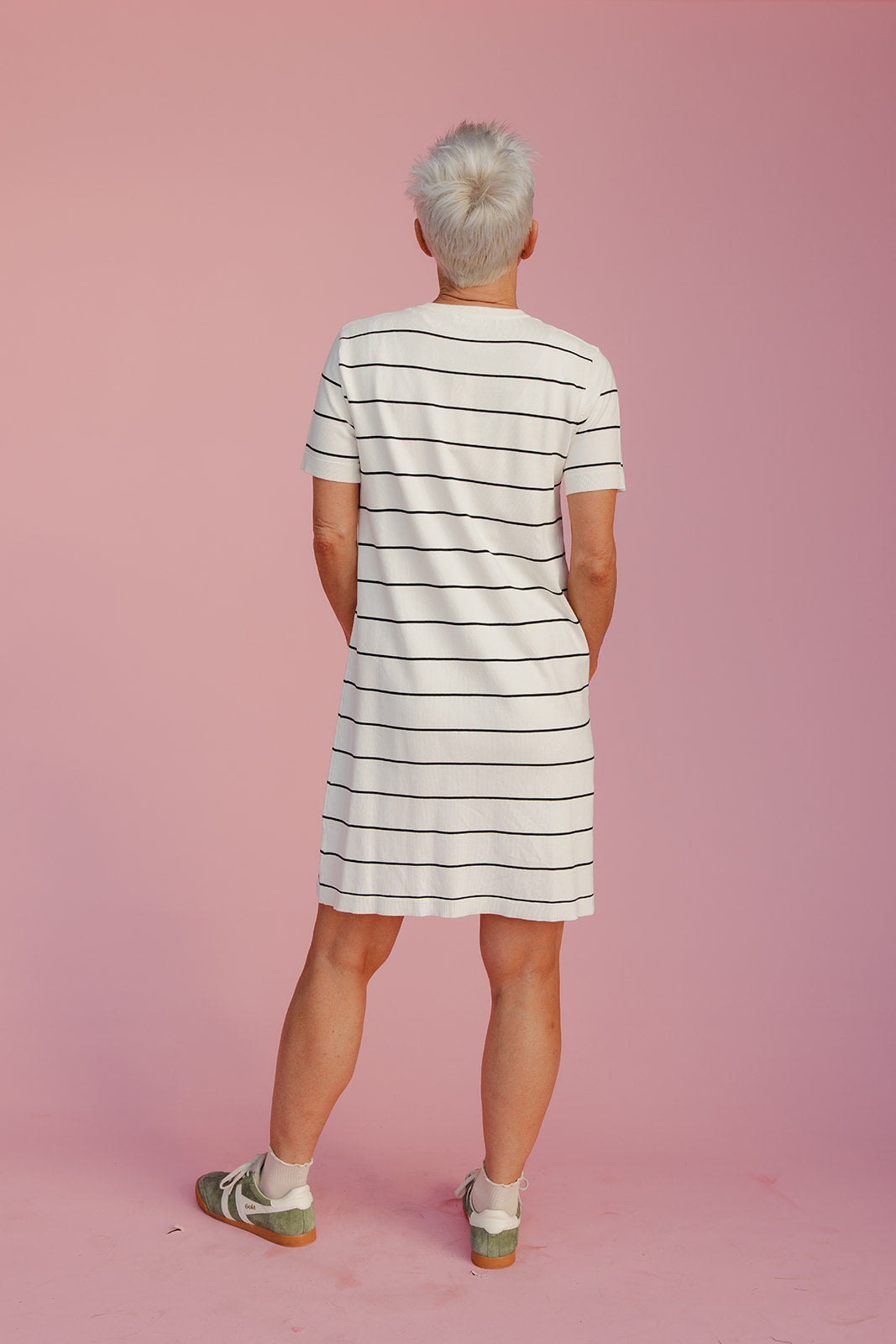 Person wearing a striped dress standing against a pink background