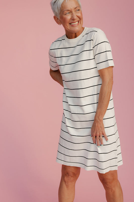 Woman wearing a white dress with black stripes against a pink background
