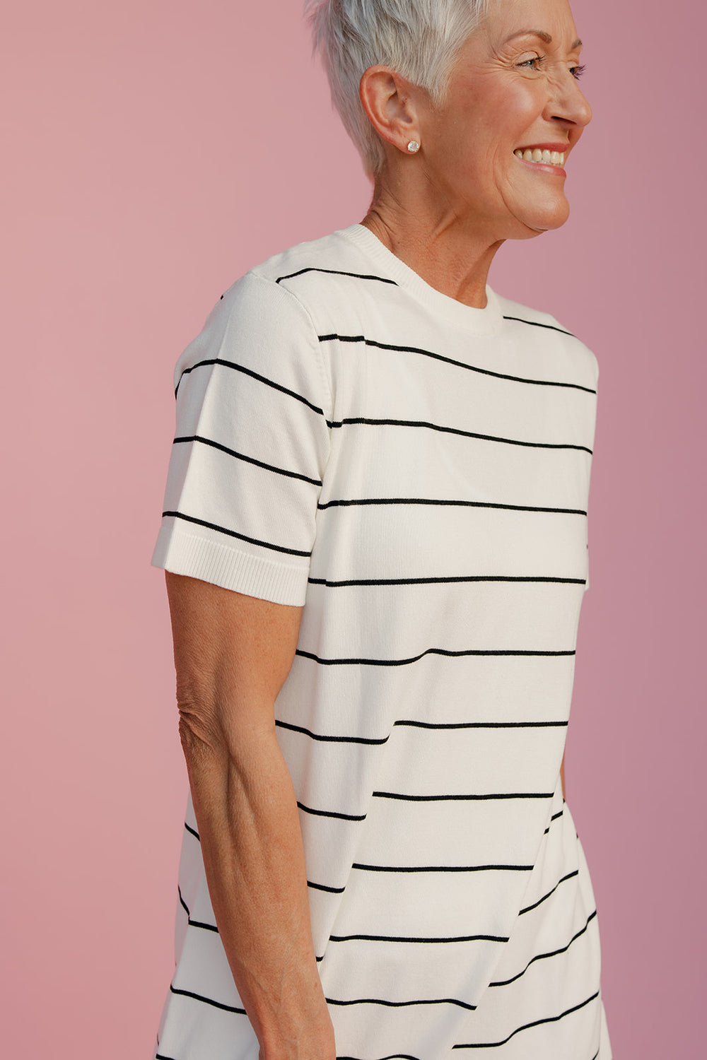 Woman wearing a white t-shirt with black stripes against a pink background
