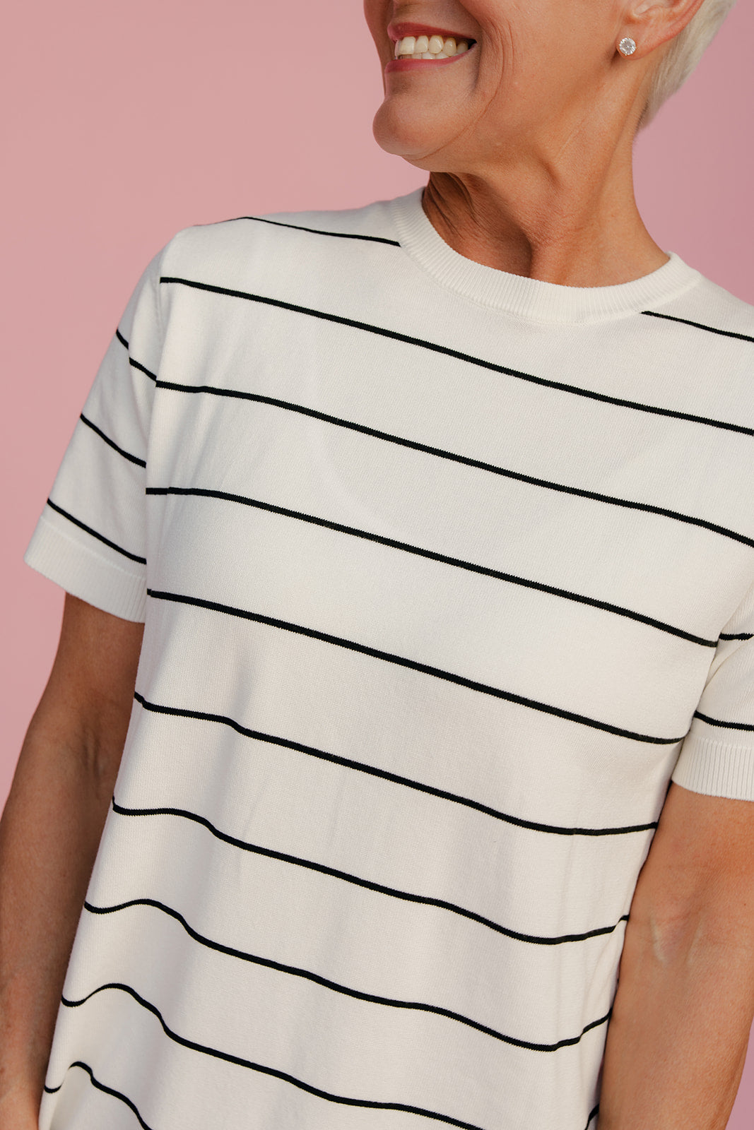 Person wearing a white t-shirt with black horizontal stripes against a pink background