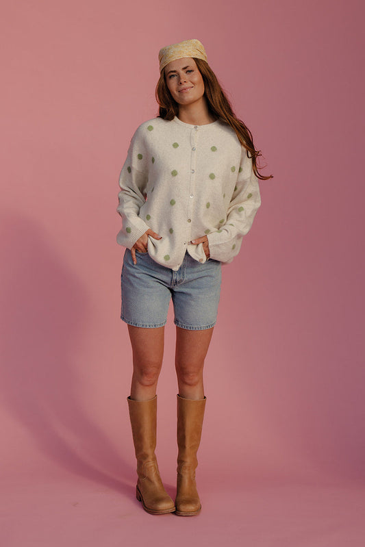 Woman wearing a patterned sweater, denim shorts, and brown boots against a pink background