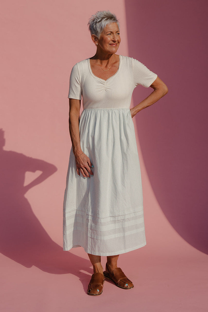 Woman in a white dress standing against a pink background