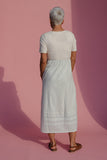 Person wearing a white outfit standing against a pink background