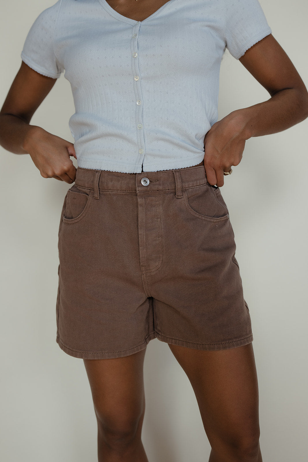 Person wearing a light blue shirt and brown shorts against a plain background