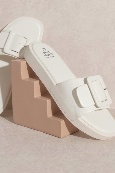 a pair of white sandals with buckles on a pink stand