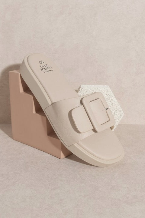 a white sandal with a buckle on a pink stand