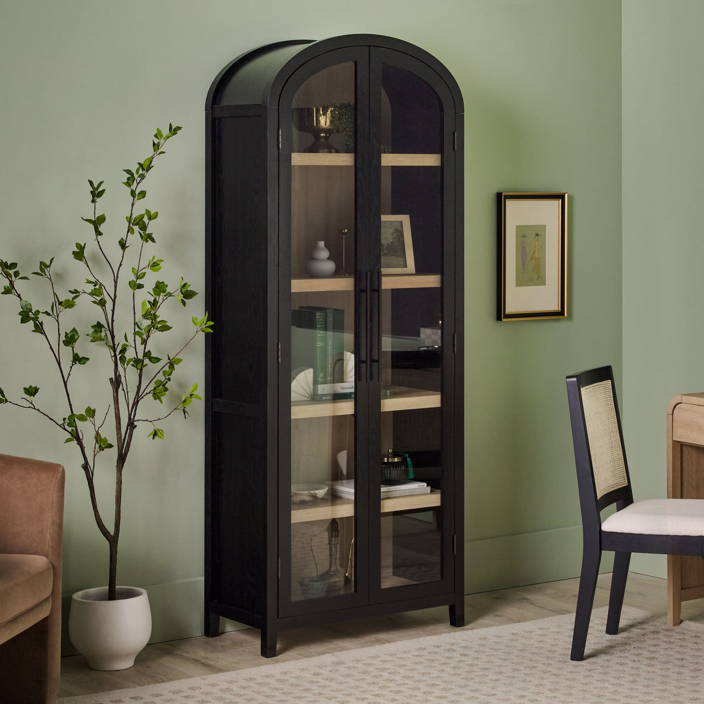 a black cabinet with glass doors and a chair in front of a green wall