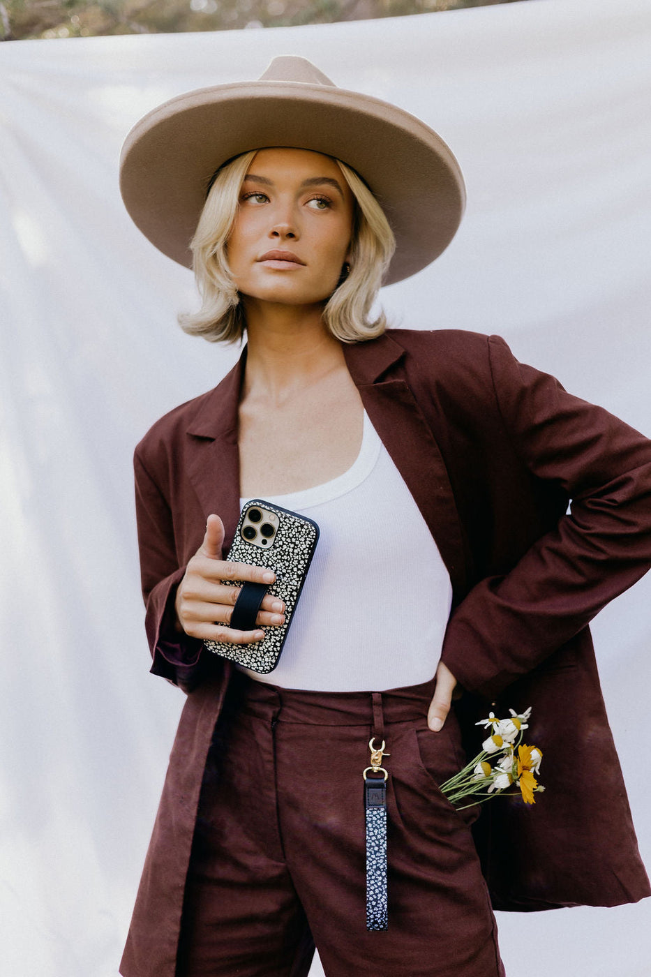 a woman in a hat holding a phone and flowers