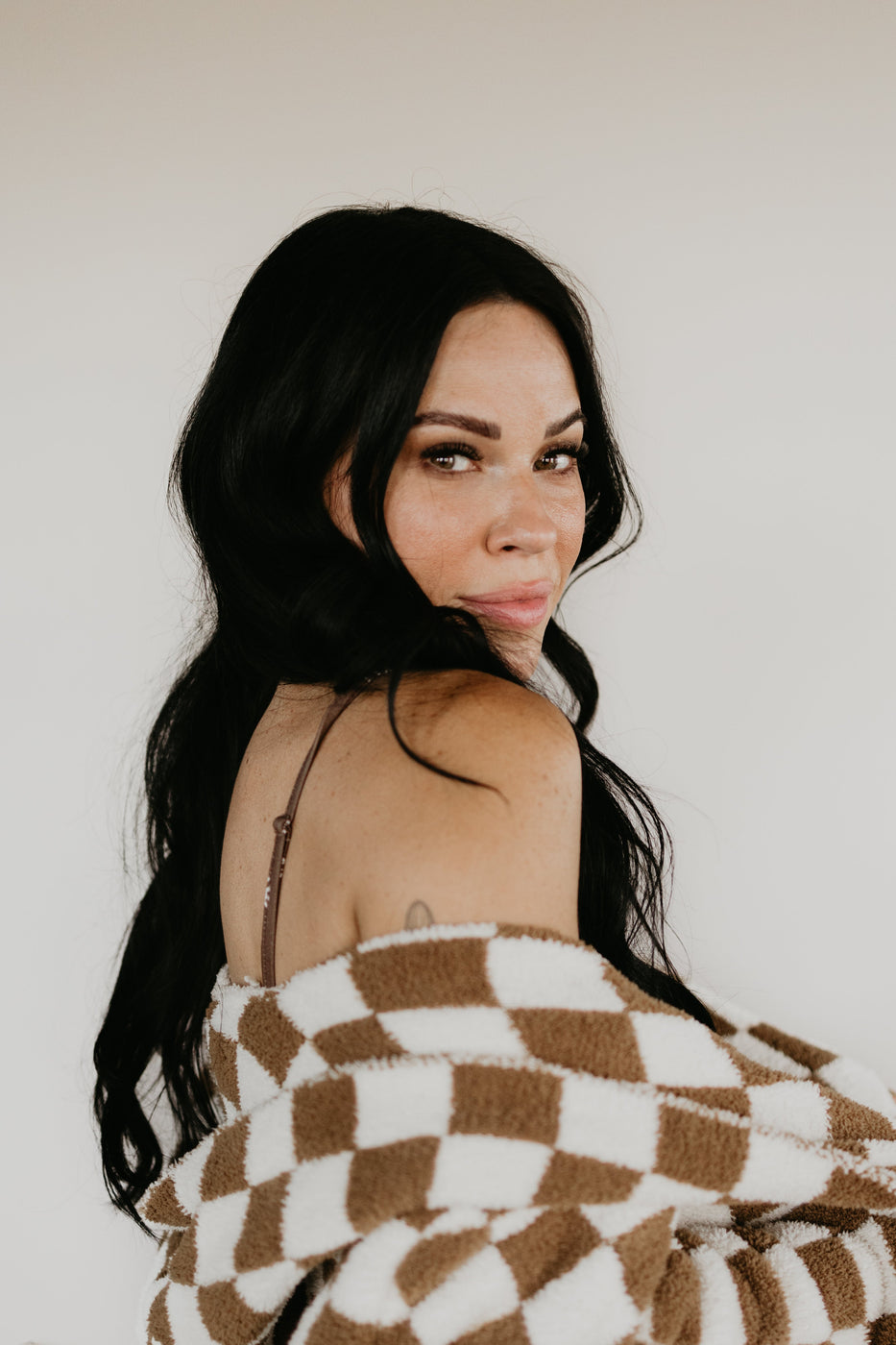 a woman with long black hair wearing a brown and white blanket