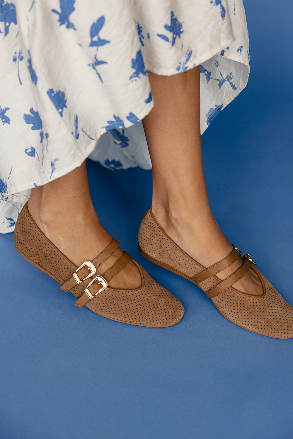 Brown sandals with buckles worn with a white floral dress on a blue background
