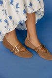 Brown sandals with buckles worn with a white floral dress on a blue background