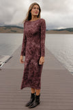 Woman in a long, burgundy dress standing on a wooden dock by a lake with mountains in the background.