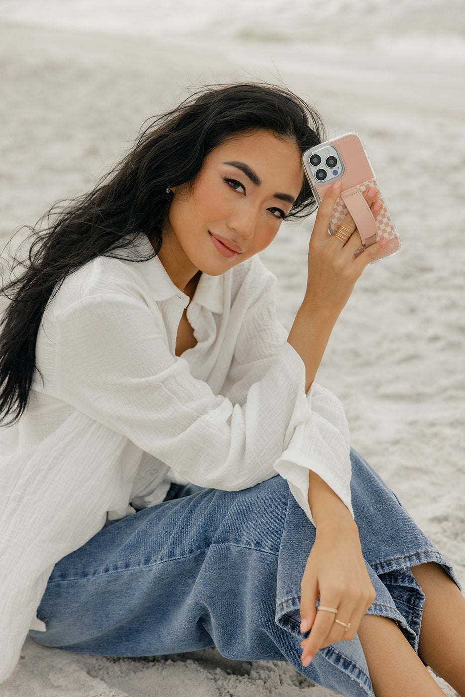 a woman sitting on sand holding a phone