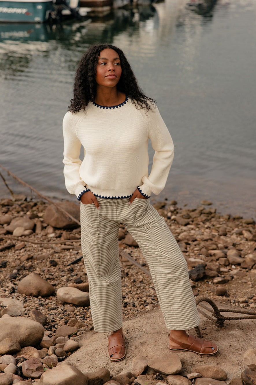 Woman standing on a rocky shore with boats in the background