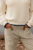 Person wearing a cream sweater with blue trim and plaid pants in an outdoor setting