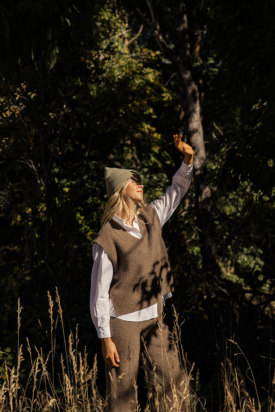 a woman in a hat and vest standing in a forest