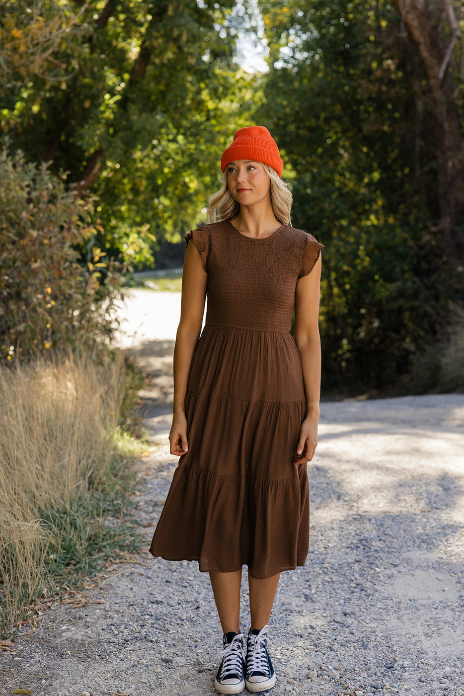 a woman in a brown dress and orange hat standing on a path