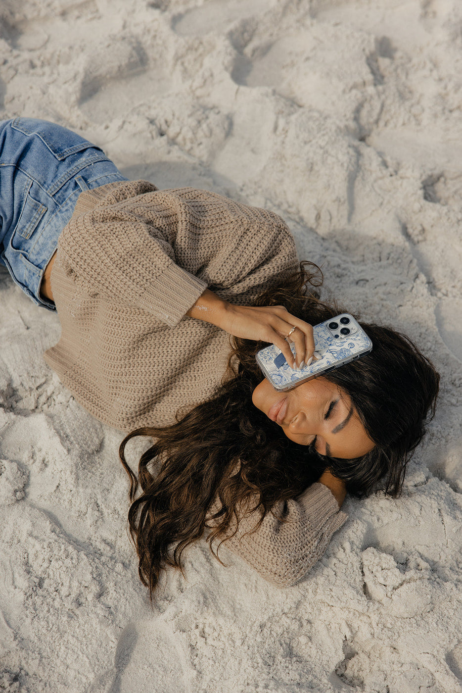 a woman lying on the sand holding a phone to her face