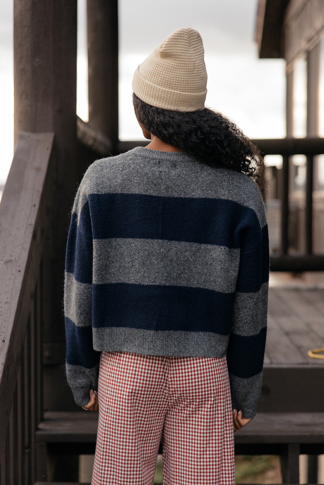 Person wearing a striped sweater and checkered pants standing on a wooden staircase.