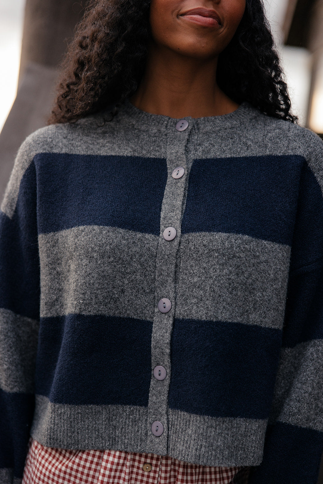 Person wearing a gray and navy striped cardigan with a blurred background