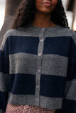 Person wearing a gray and navy striped cardigan with a blurred background