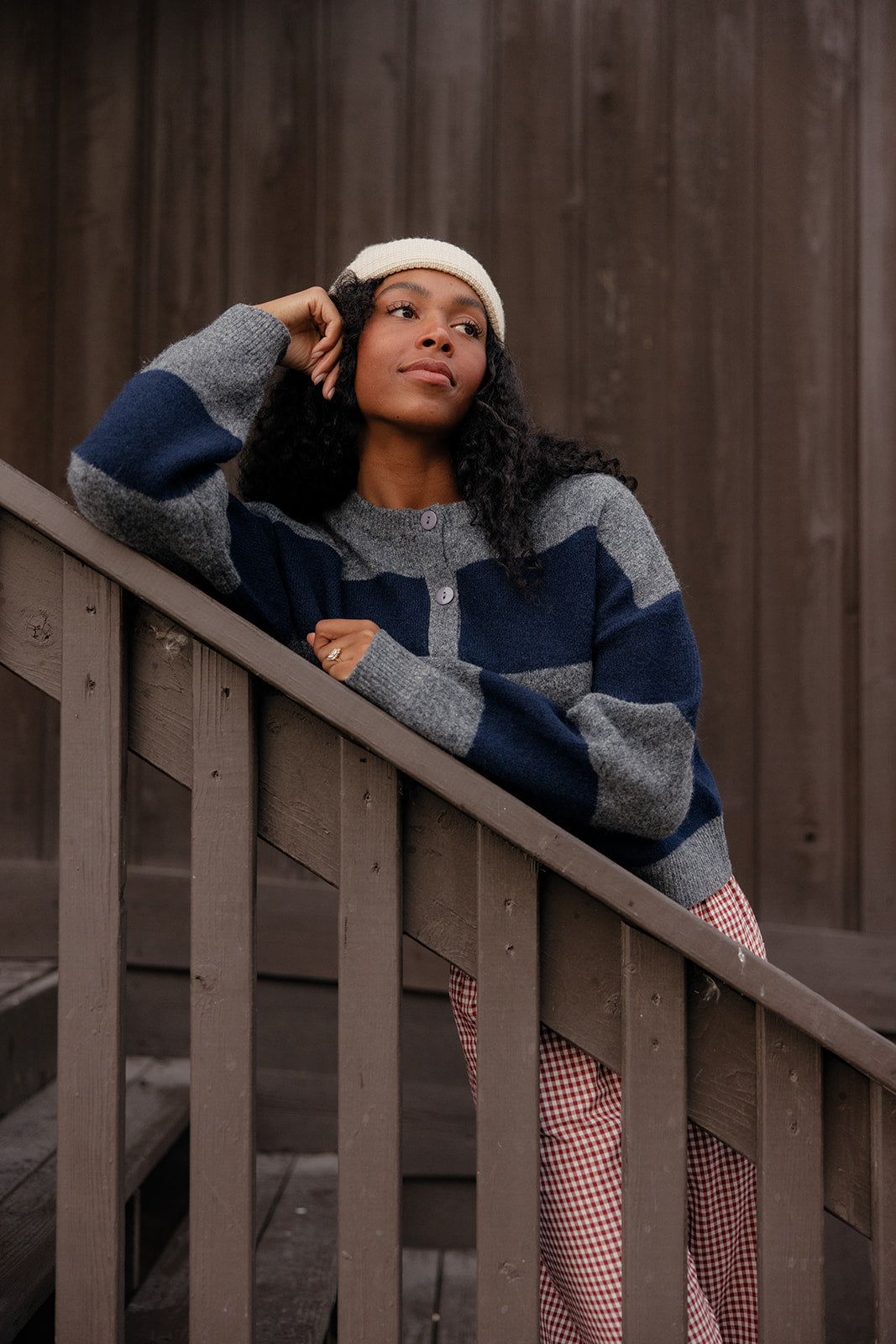 Woman in a blue and gray striped sweater and plaid pants standing on wooden steps.
