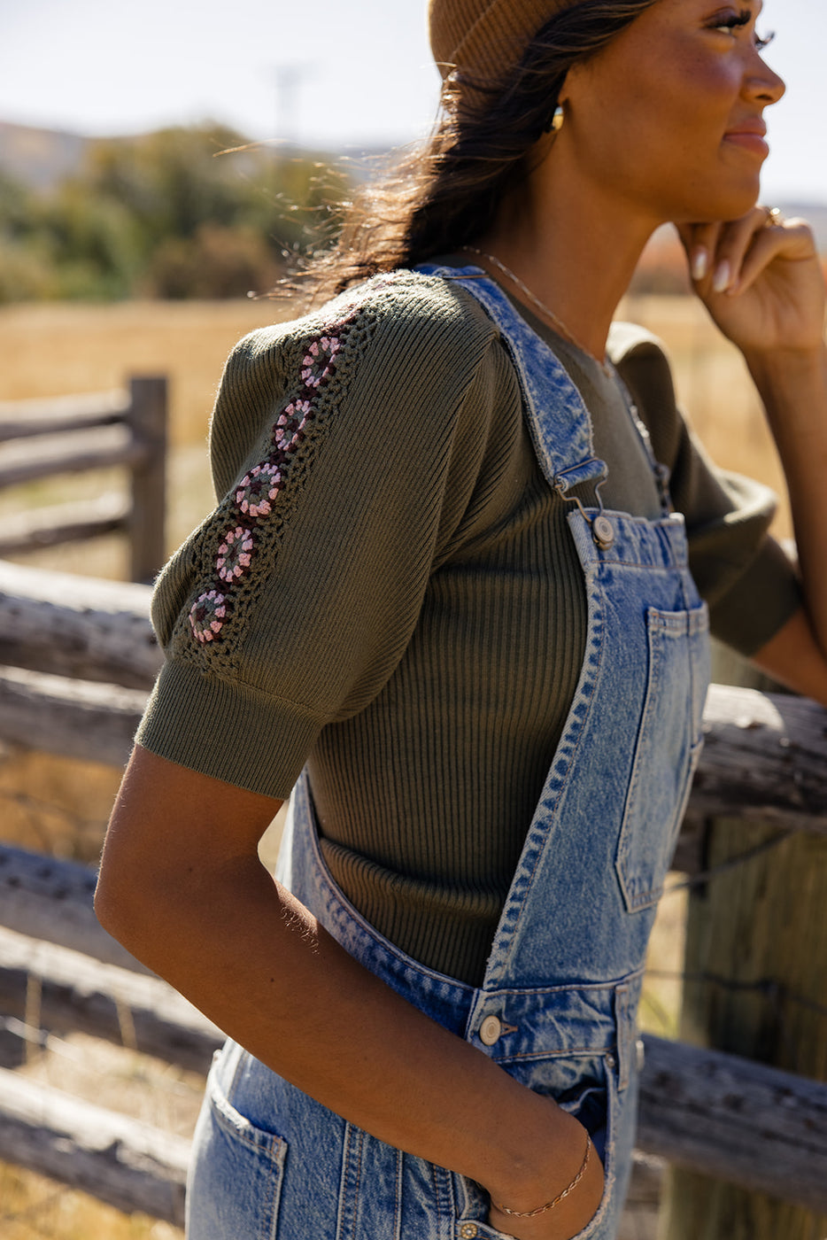 a woman in overalls standing by a fence