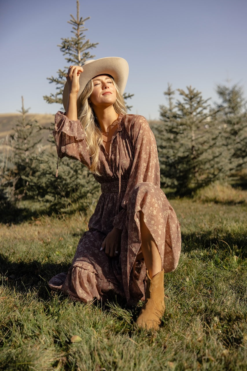 a woman in a dress and cowboy hat kneeling in grass