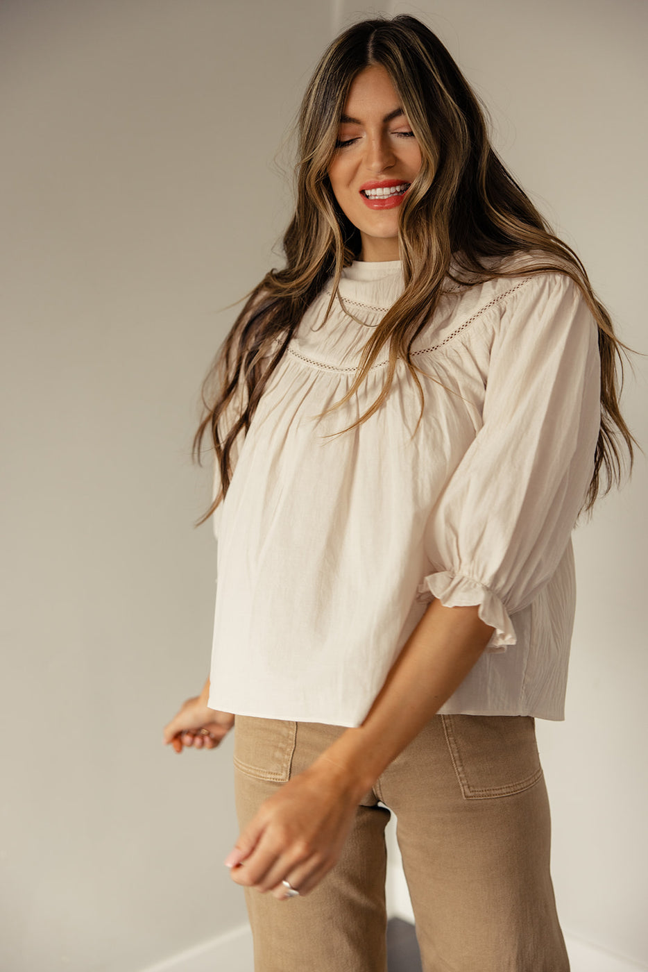 a woman with long hair wearing a white shirt and brown pants